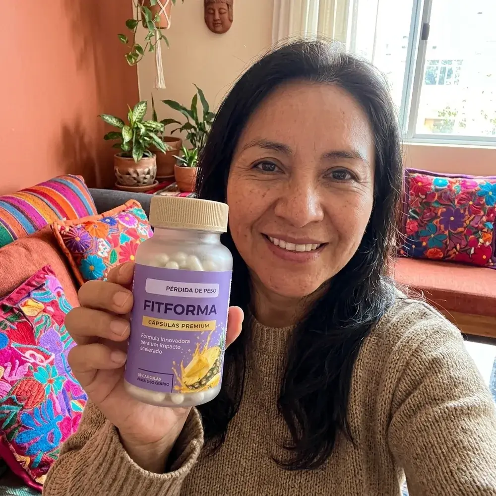 Mujer de 51 años sonriente mostrando el frasco de FitForma en la sala de su casa